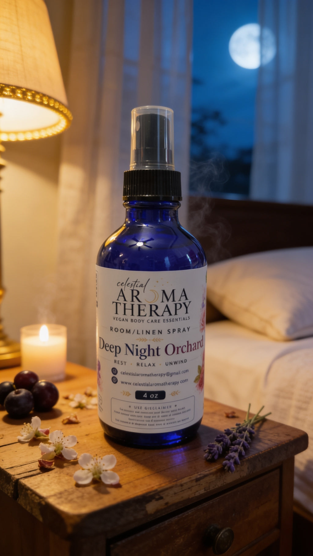 A cobalt blue glass room and linen spray bottle by Sacred Arma Therapy sits on a rustic wooden nightstand in a cozy bedroom setting. The bottle is labeled 'Deep Night Orchid' and is styled with a lit candle, fresh lavender sprigs, and dark grapes, with a warm lamp glowing in the background.